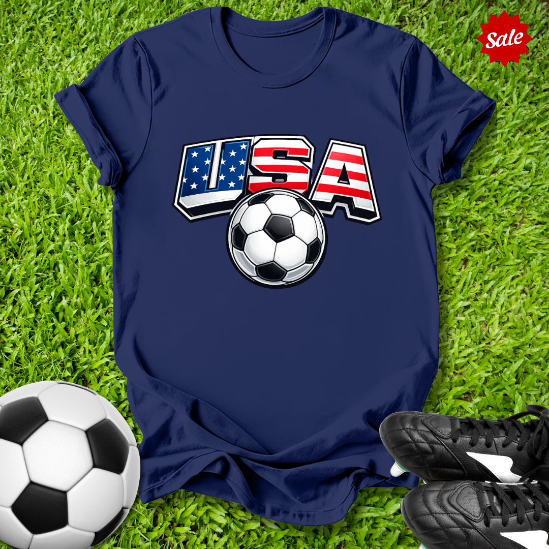 Navy blue t-shirt with USA soccer design on grass with soccer ball and shoes.