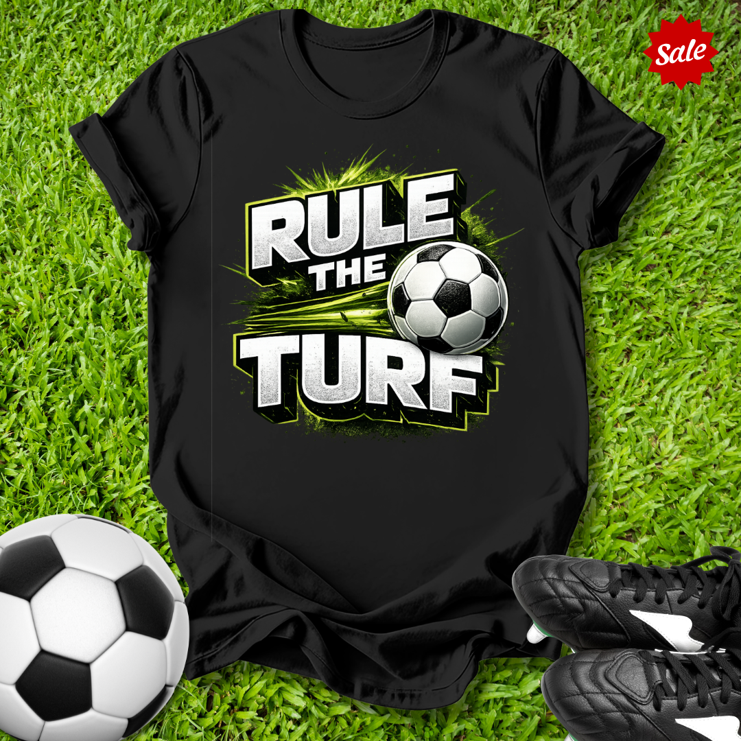 Black t-shirt with 'Rule the Turf' design on grass with soccer ball and shoes.
