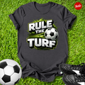 Dark gray t-shirt with 'Rule the Turf' design on grass with soccer ball and shoes.