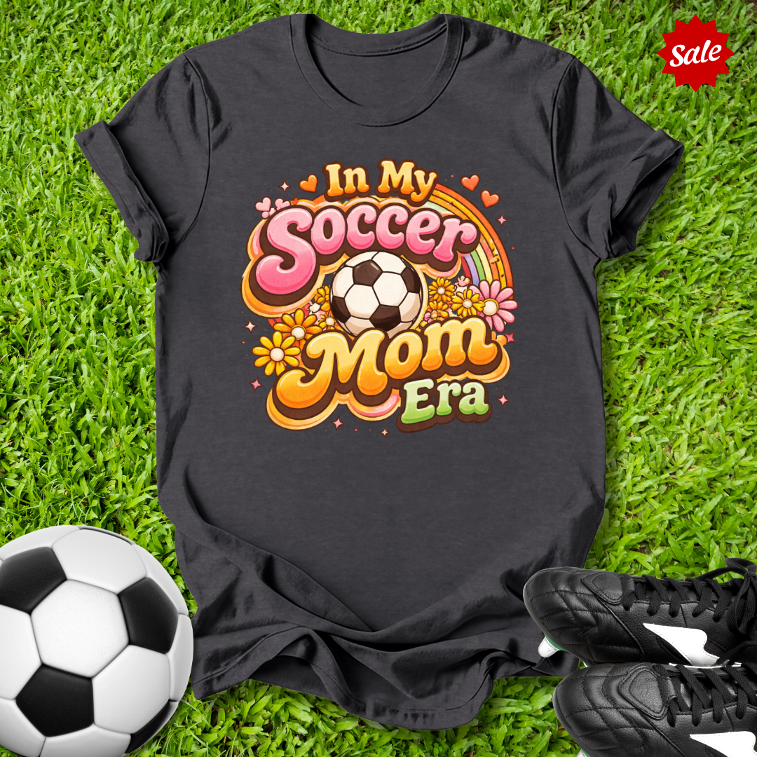 Black t-shirt with 'In My Soccer Mom Era' design on grass with soccer ball and shoes.
