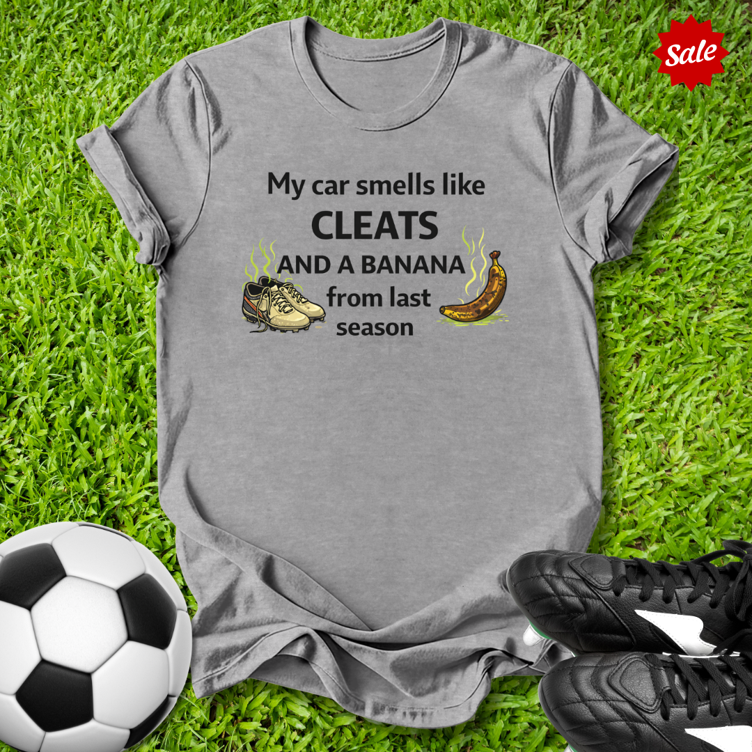 Gray t-shirt with humorous  my car smells like cleats and a banana from last season text about car smell, soccer ball, and cleats on grass