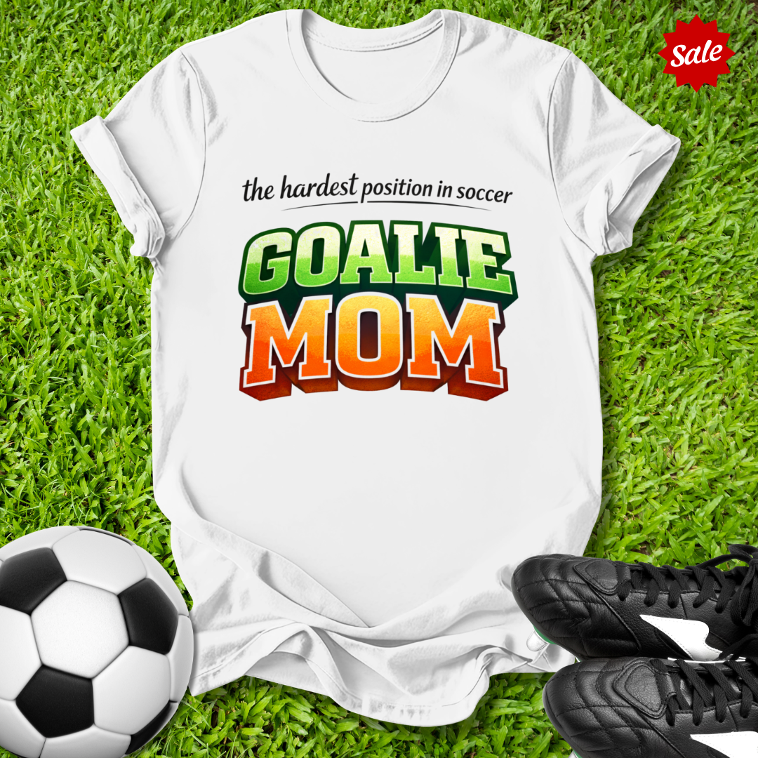 White t-shirt with 'GOALIE MOM' text on grass with soccer ball and cleats