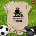 Beige t-shirt with 'My Weekend Throne' graphic on grass with soccer ball and shoes.
