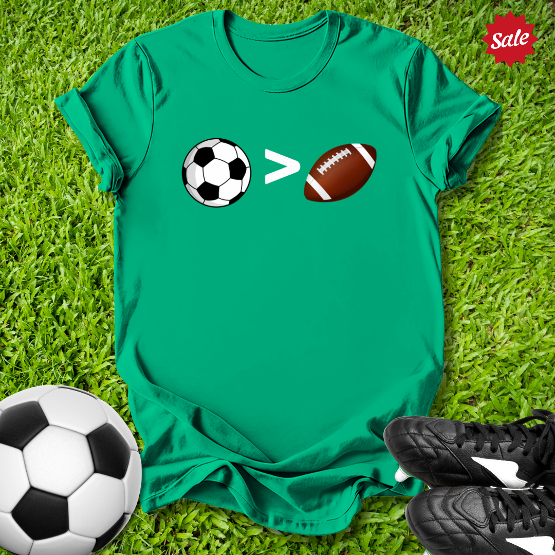 Green t-shirt with sports-themed design on grass, surrounded by soccer ball and football