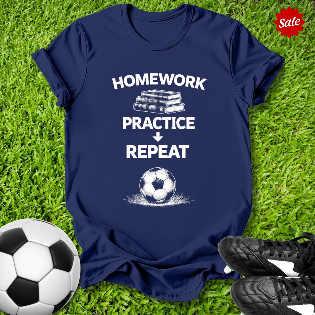 Navy blue t-shirt with 'Homework Practice Repeat' text and soccer ball graphic on grass with soccer ball and shoes.