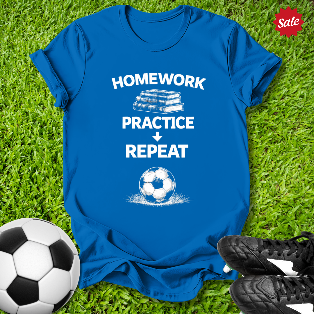 Blue t-shirt with 'Homework Practice Repeat' text on grass with soccer ball and shoes