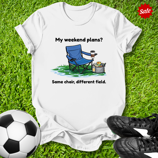 White t-shirt with a graphic and text on grass with soccer ball and shoes