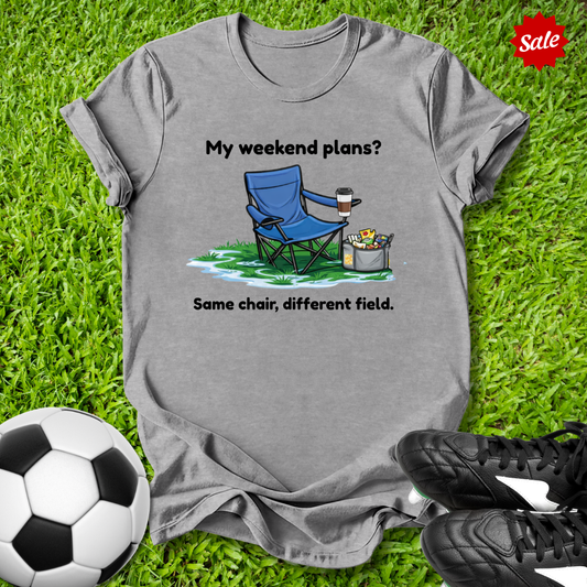 Gray t-shirt with a graphic and text on grass with soccer ball and shoes