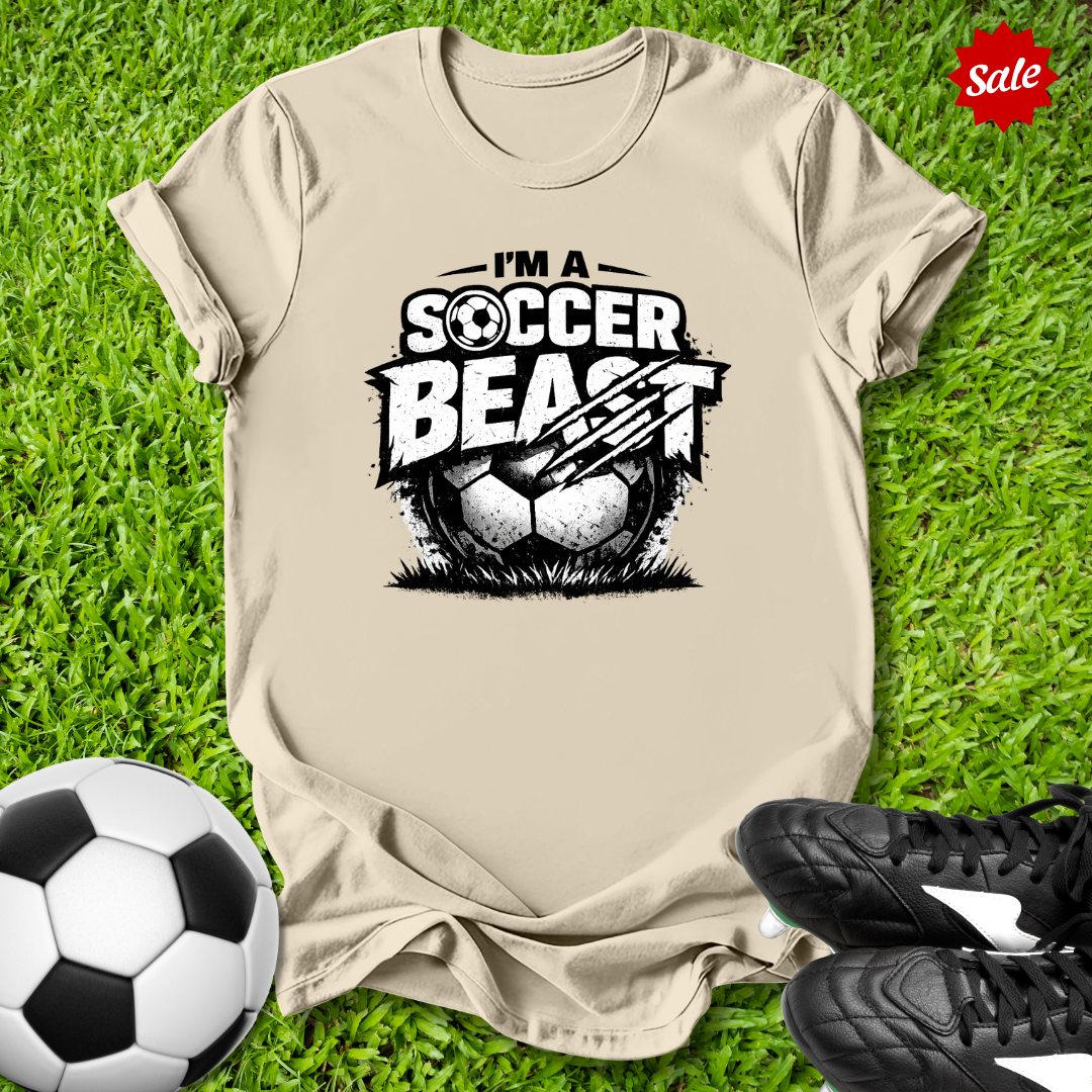 Beige t-shirt with 'Soccer Beast' graphic on grass with soccer ball and shoes.