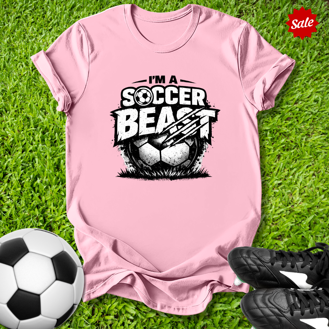 Pink t-shirt with 'Soccer Beast' graphic on grass with soccer ball and shoes