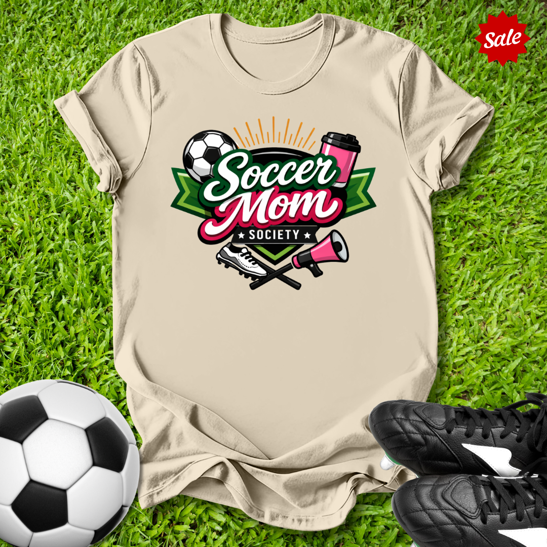 Beige t-shirt with 'Soccer Mom Society' design on grass with soccer ball and shoes.