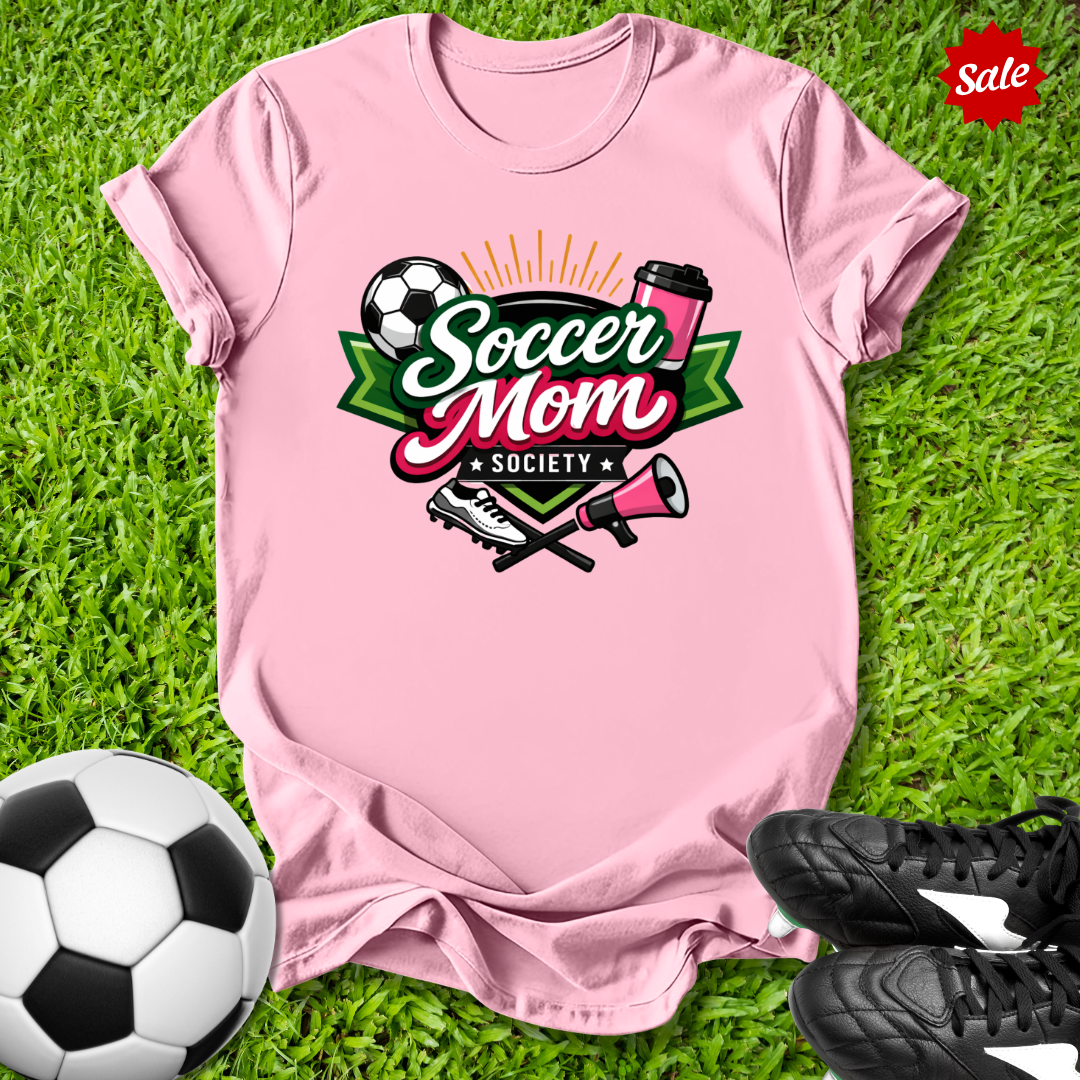 Pink t-shirt with 'Soccer Mom Society' design on grass with soccer ball and shoes.
