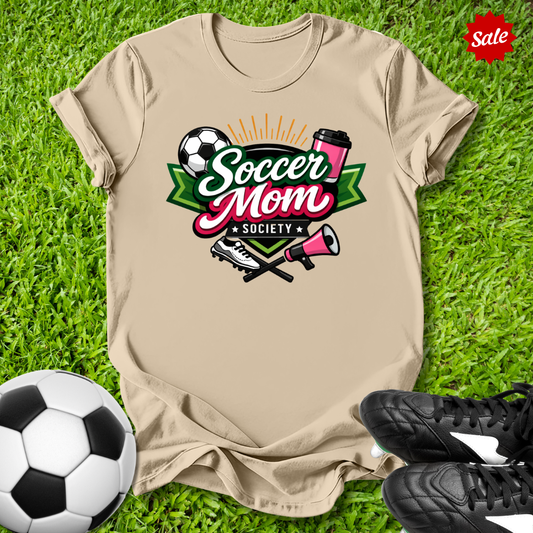 Beige t-shirt with 'Soccer Mom Society' design on grass with soccer ball and shoes.