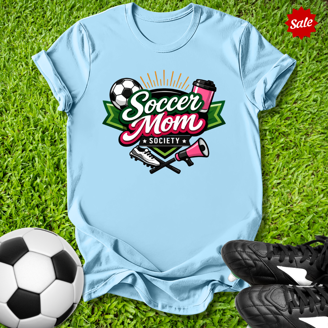 Light blue t-shirt with 'Soccer Mom Society' design on grass with soccer ball and shoes.