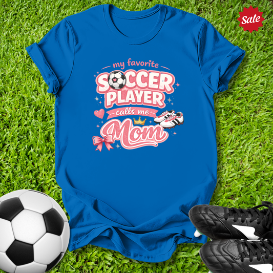 Blue t-shirt with soccer-themed design  and My Favorite Player Calls Me Mom text on grass with soccer ball and shoes