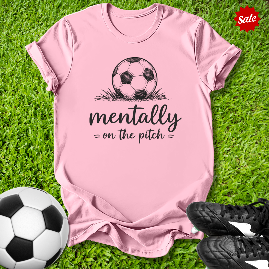 Pink t-shirt with soccer ball graphic and text on grass with soccer ball and shoes