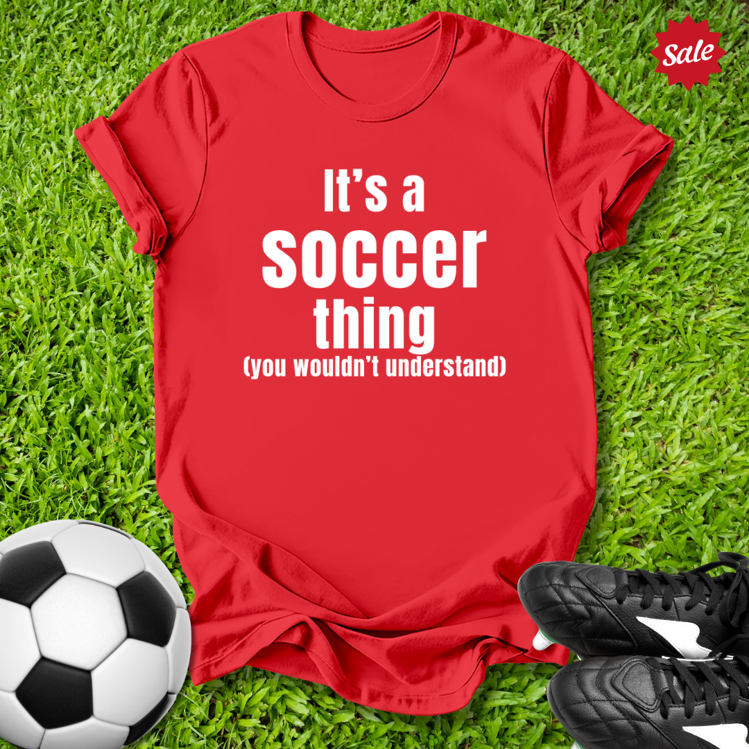 Red t-shirt with 'It's a Soccer Thing ,You Wouldn't Understand' text on grass with soccer ball and shoes