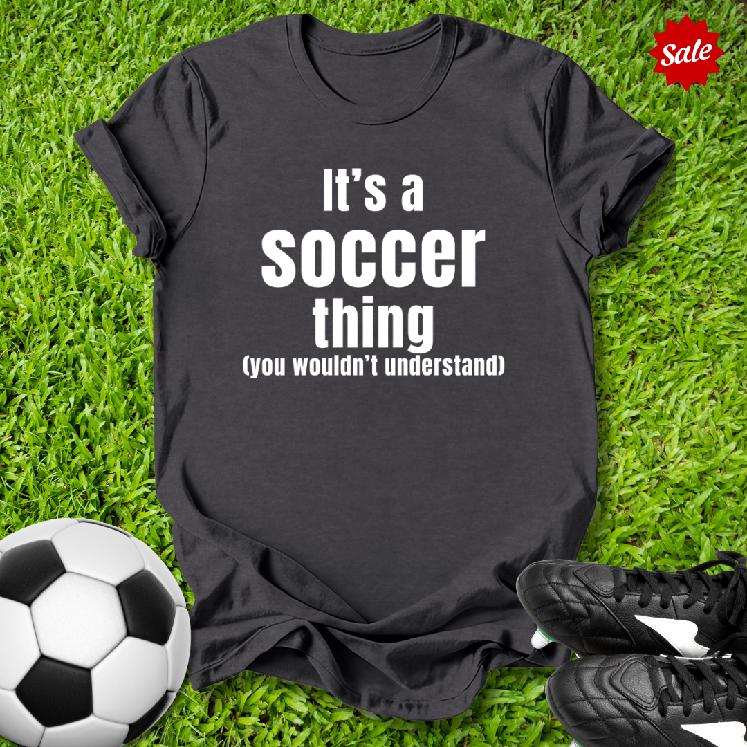 Gray t-shirt with 'It's a Soccer Thing ,You Wouldn't Understand' text on grass with soccer ball and shoes