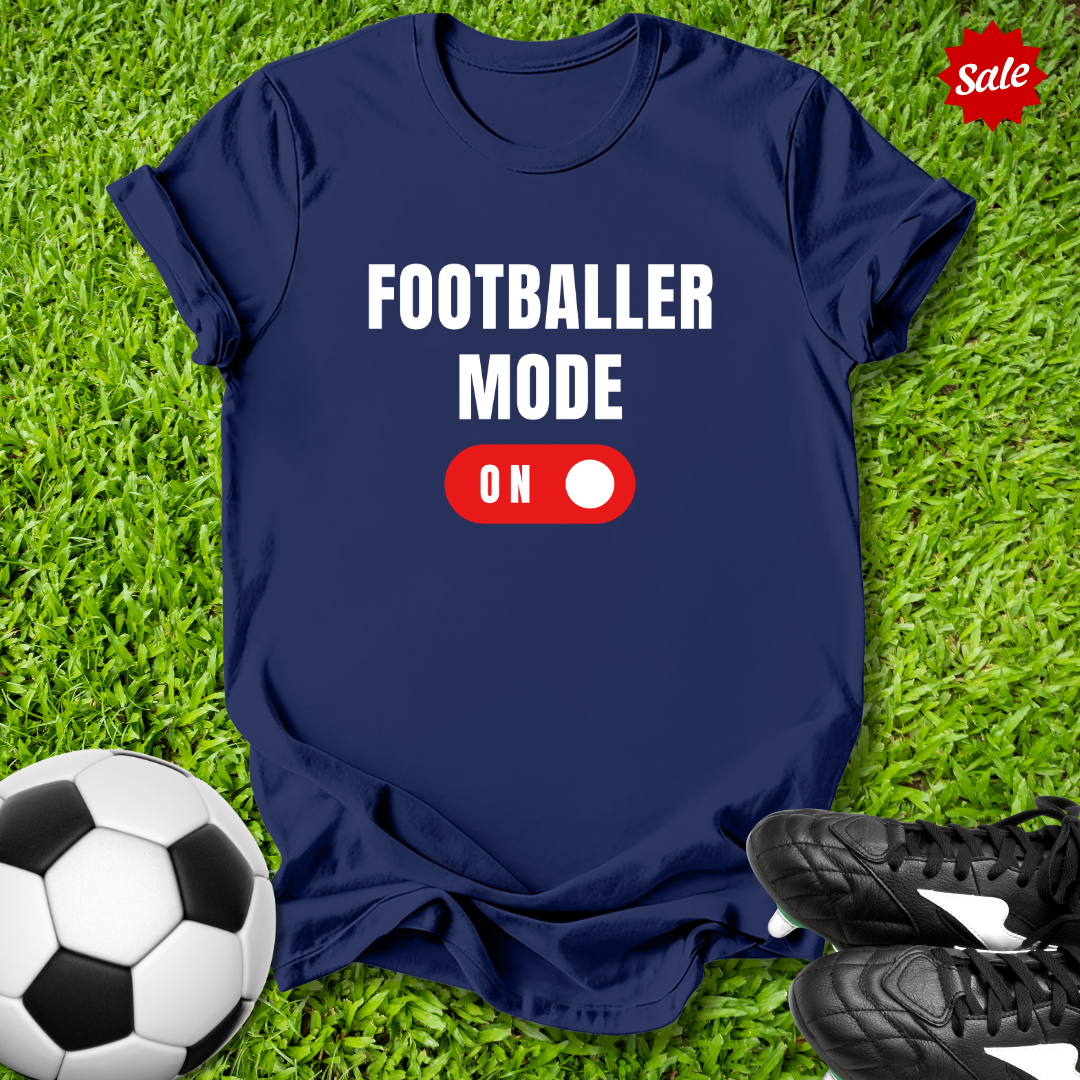 Blue  t-shirt with 'Footballer Mode On' text on grass with soccer ball and shoes
