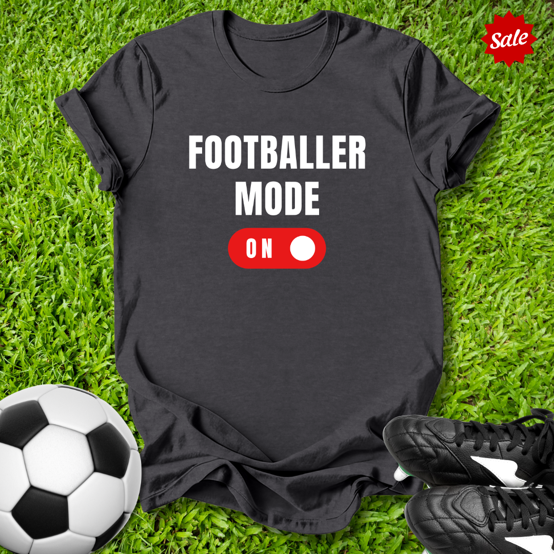 Gray  t-shirt with 'Footballer Mode On' text on grass with soccer ball and shoes