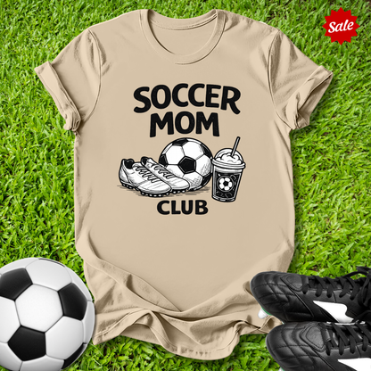Beige Pink t-shirt with 'Soccer Mom Club' text on grass with soccer ball and shoes