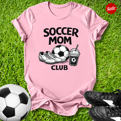 Pink t-shirt with 'Soccer Mom Club' text on grass with soccer ball and shoes