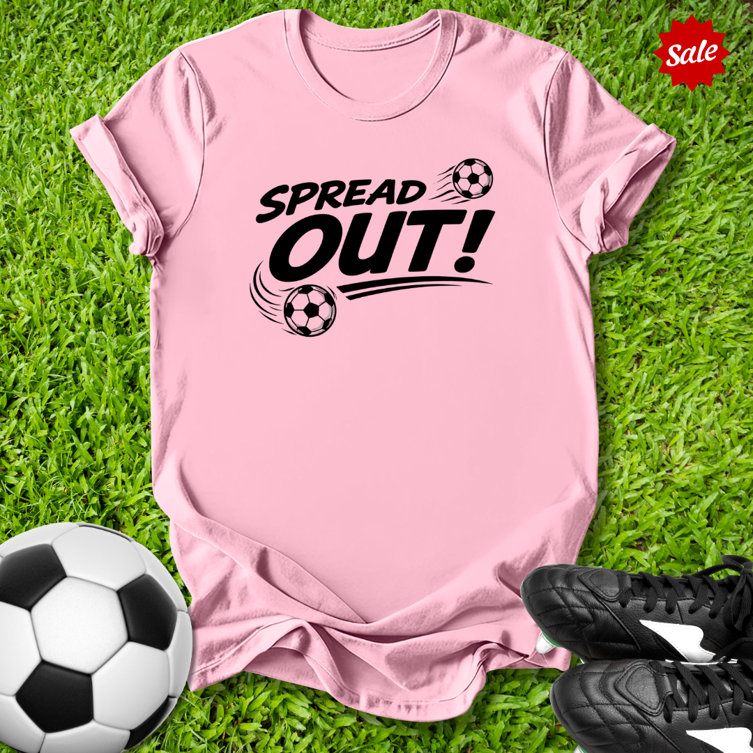 Pink t-shirt with 'Spread Out!' text and soccer ball graphics on grass with soccer ball and shoes.