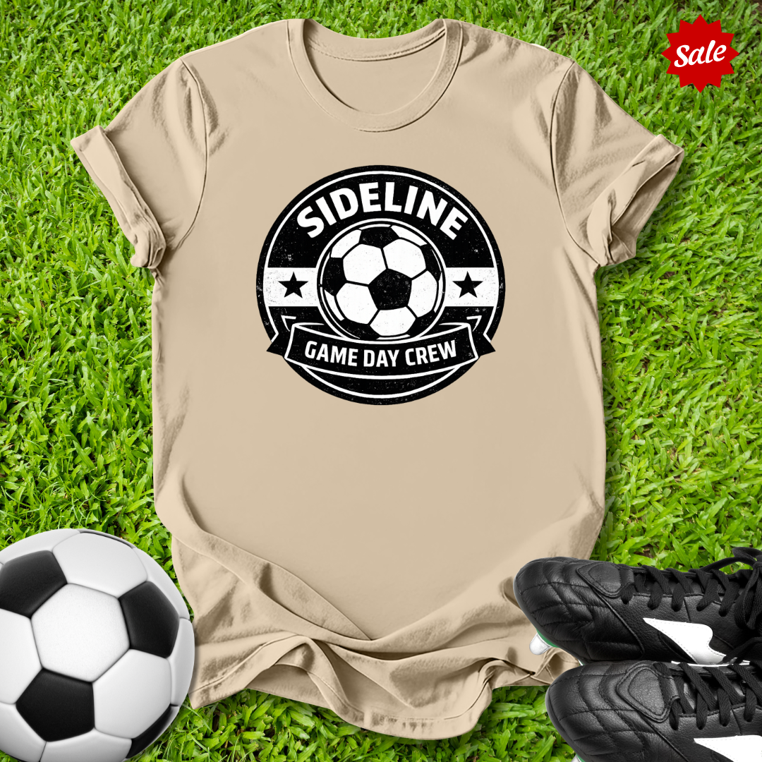 Beige t-shirt with soccer-themed design on grass with soccer ball and shoes