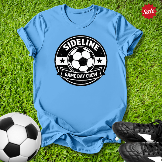 Blue t-shirt with 'Sideline Game Day Crew' design on grass with soccer ball and shoes.