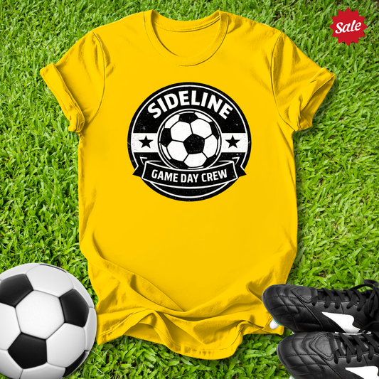 Yellow t-shirt with 'Sideline Game Day Crew' design on grass with soccer ball and shoes.