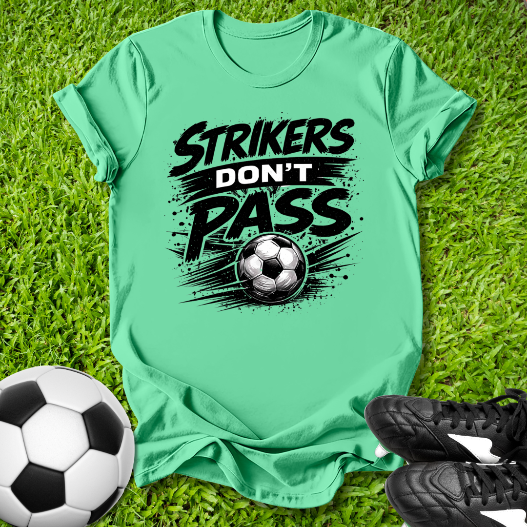 Mint green t-shirt with 'Strikers Don't Pass' text and soccer ball graphic on grass with soccer ball and shoes.