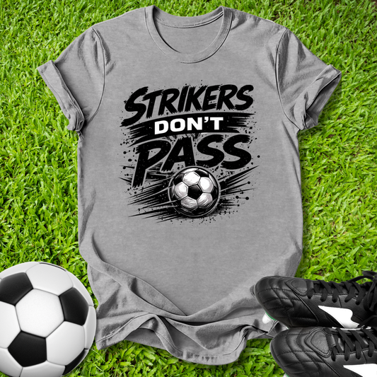 Gray t-shirt with 'Strikers Don't Pass' graphic on grass with soccer balls and shoes.