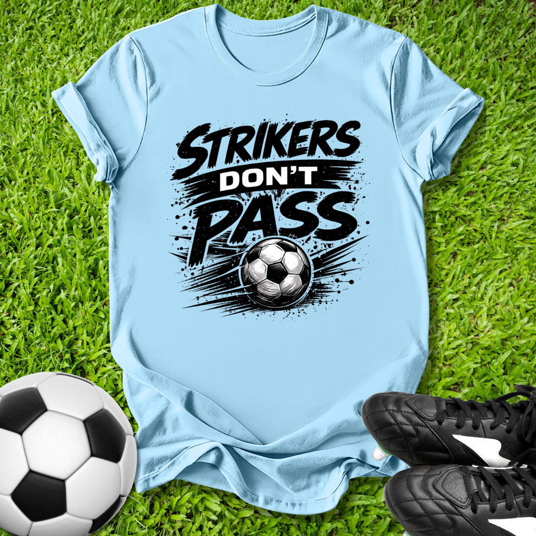Light blue t-shirt with 'Strikers Don't Pass' graphic on grass with soccer ball and shoes.