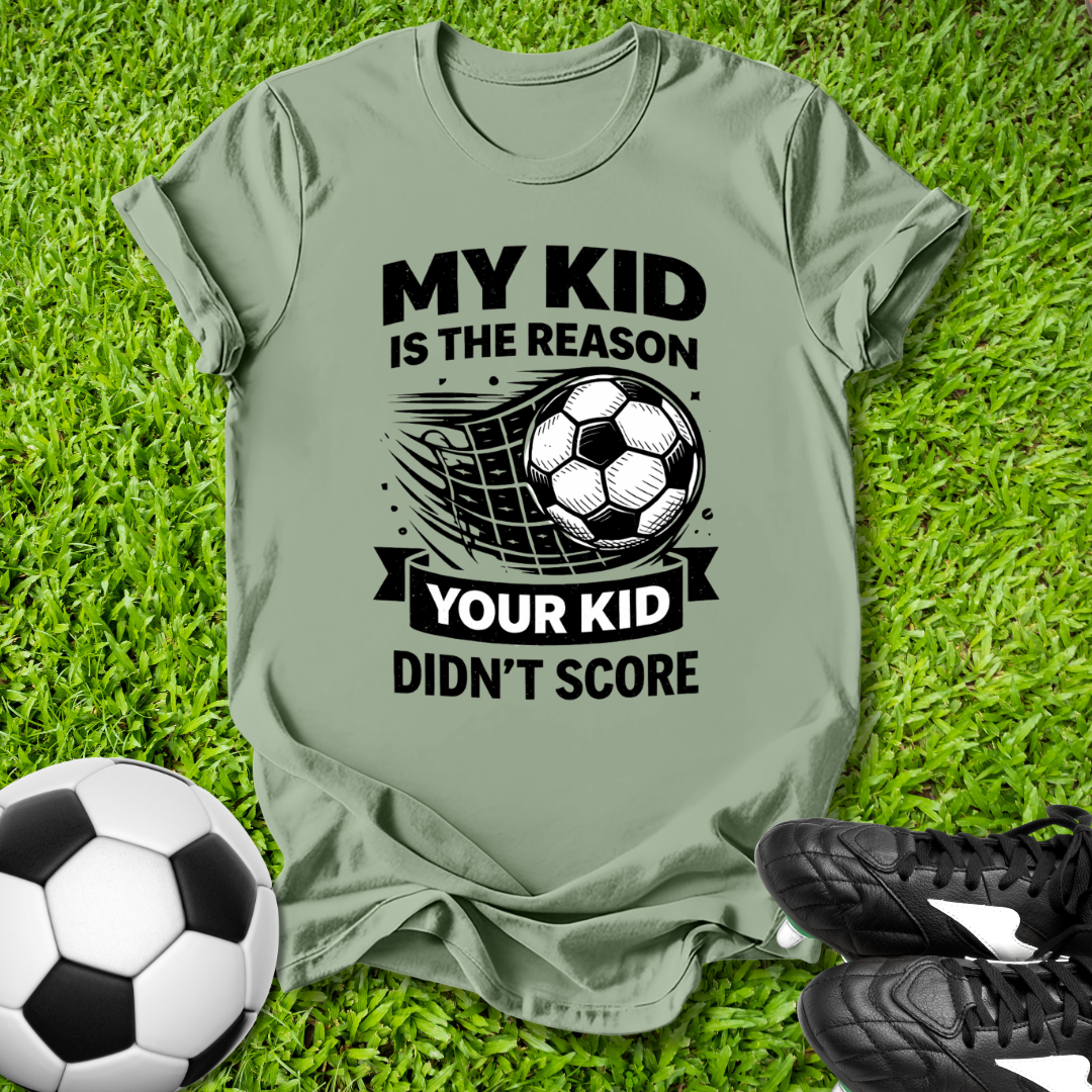 Green t-shirt with soccer-themed text on grass with soccer ball and shoes