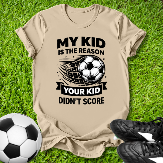 Beige t-shirt with soccer-themed text on grass with soccer ball and shoes