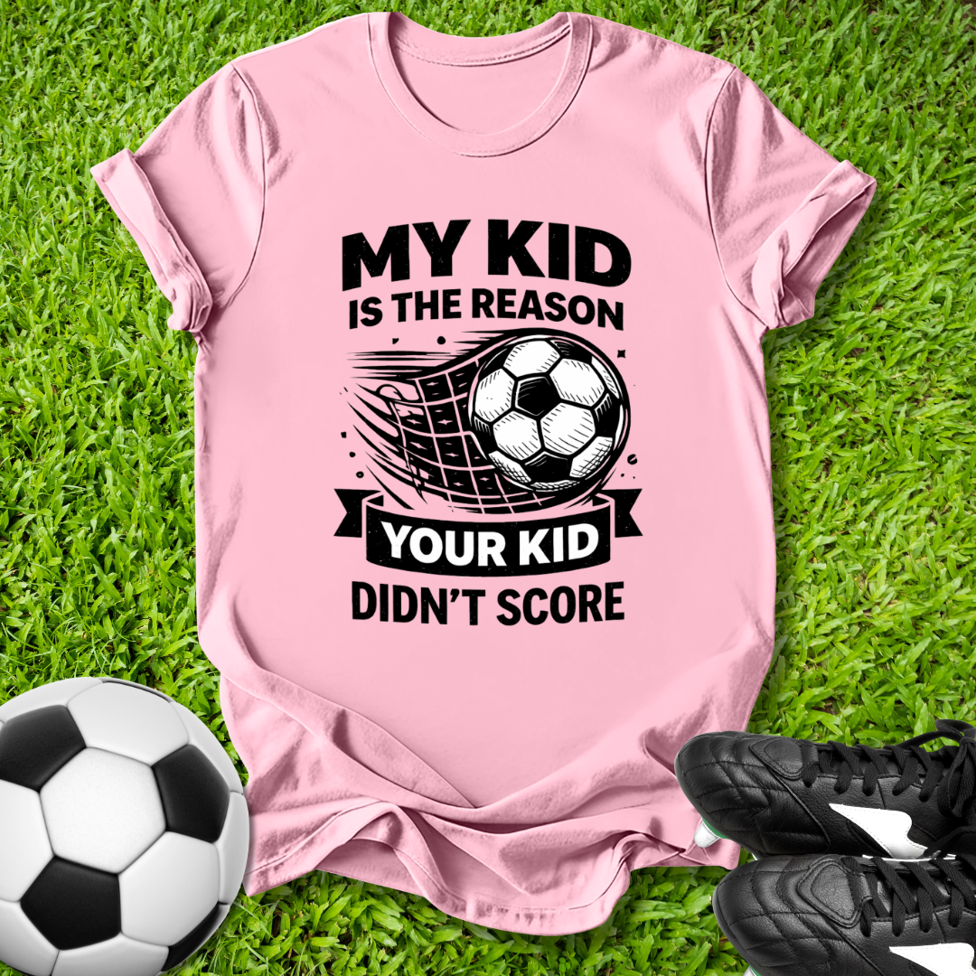 Pink t-shirt with soccer-themed text on grass with soccer ball and shoes