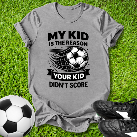 Gray t-shirt with soccer-themed text on grass with soccer ball and shoes