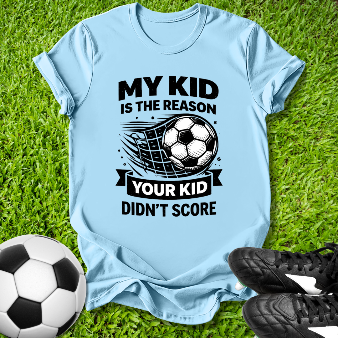 Light blue t-shirt with soccer-themed text on grass with soccer ball and shoes.