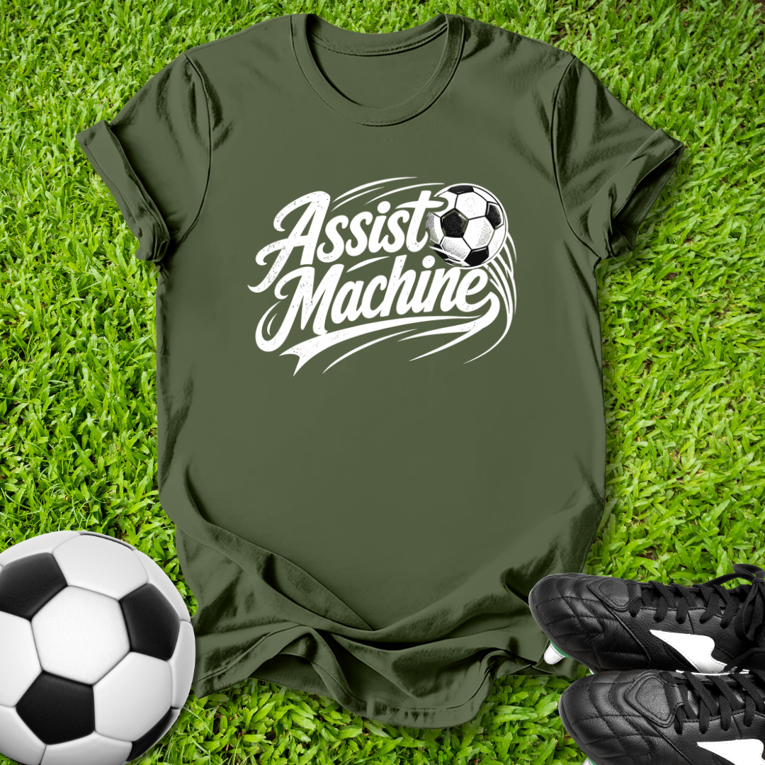 Green t-shirt with 'Assist Machine' text and soccer ball graphic on grass with soccer ball and shoes.