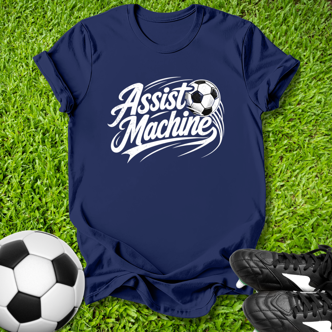 Navy blue t-shirt with 'Assist Machine' graphic on grass with soccer ball and shoes