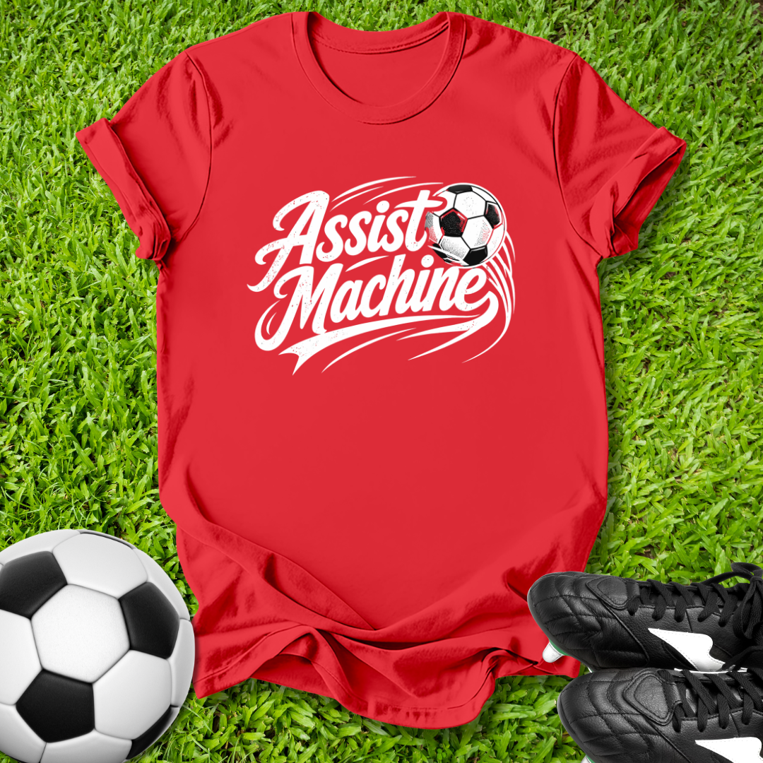 Red t-shirt with 'Assist Machine' graphic on grass with soccer balls and shoes.