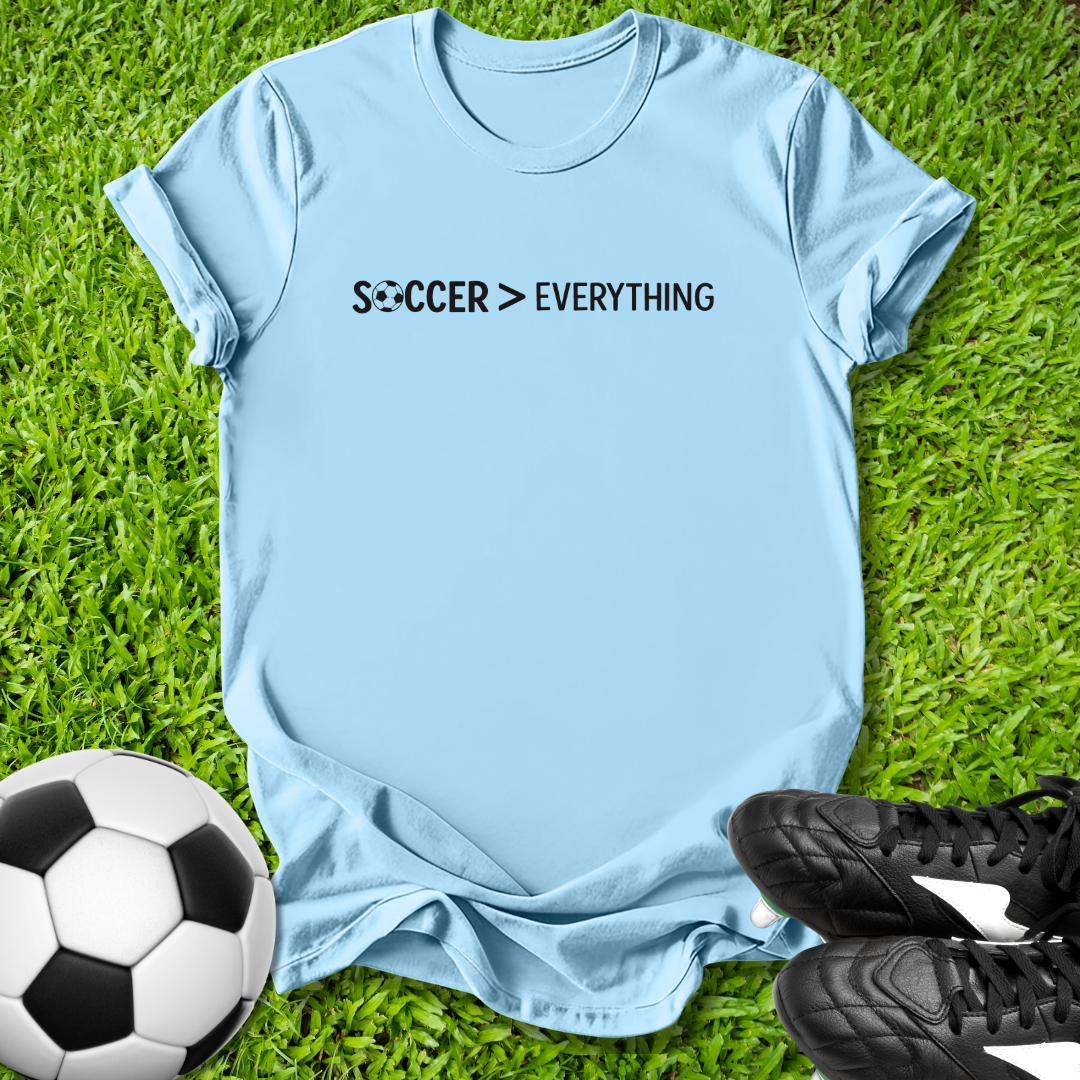 Light blue t-shirt with 'Soccer > Everything' text on grass with soccer ball and shoes.
