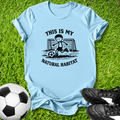 Light blue t-shirt with soccer graphic and this is my natural habitat text on grass with soccer ball and shoes.
