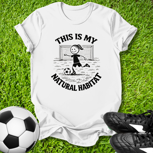 White t-shirt with soccer-themed  this is my natural habitat graphic and text on grass with soccer ball and shoes.