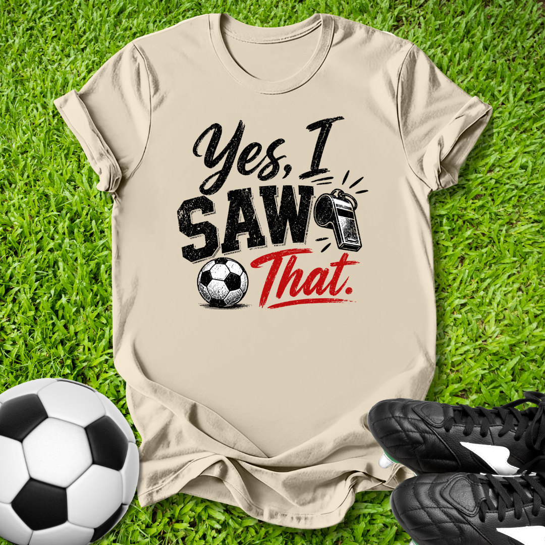 Beige t-shirt with 'Yes, I Saw That' text on grass with soccer ball and shoes