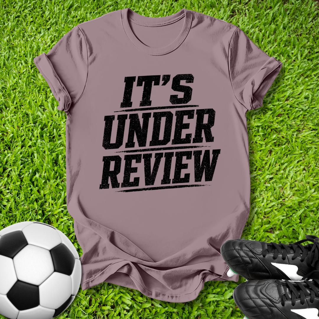 T-shirt with 'It's Under Review' text on grass with soccer ball and shoes