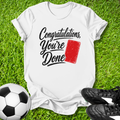 White t-shirt with 'Congratulations, You're Done' text and red card on grass with soccer ball and shoes.