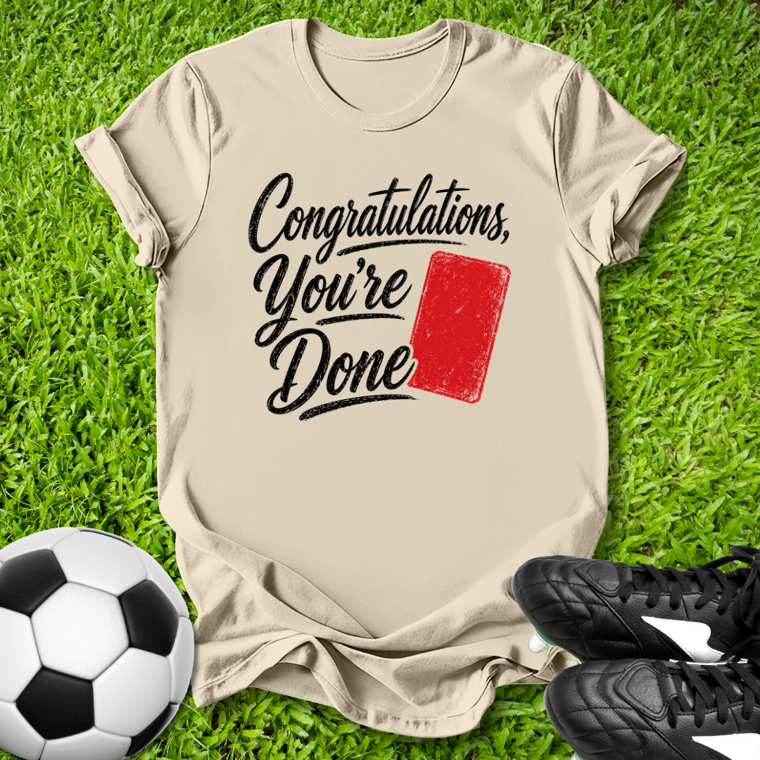 Beige t-shirt with 'Congratulations, You're Done' text and red card graphic on grass with soccer ball and shoes.
