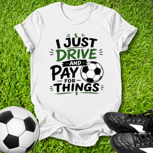 White t-shirt with soccer-themed I just drive and pay for things text on grass with soccer ball and shoes
