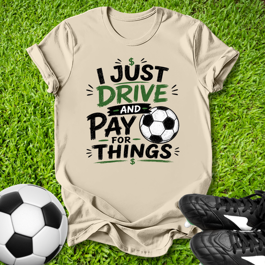 Beige t-shirt with soccer-themed I just drive and pay for things text on grass with soccer ball and shoes